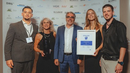 Fünf Vertreter des Hotels Der Blaue Reiter stehen bei der Preisverleihung mit Pokal und Urkunde vor einer Sponsorenwand.