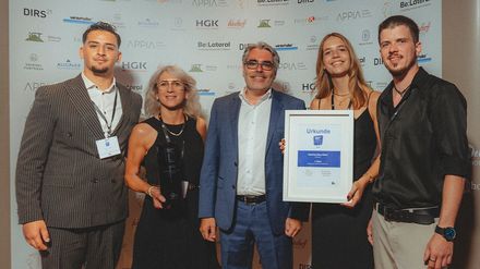 Fünf Vertreter des Hotels Der Blaue Reiter stehen bei der Preisverleihung mit Pokal und Urkunde vor einer Sponsorenwand.