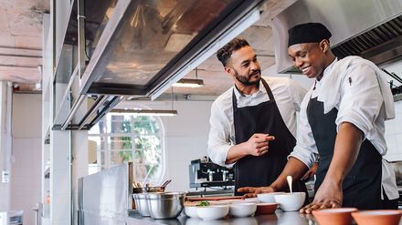 Zwei Köche bereiten gemeinsam Speisen in einer professionellen Restaurantküche zu.