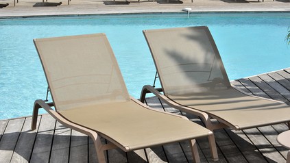Zwei leere Sonnenliegen stehen auf einer Holzterrasse direkt an einem Hotelpool.