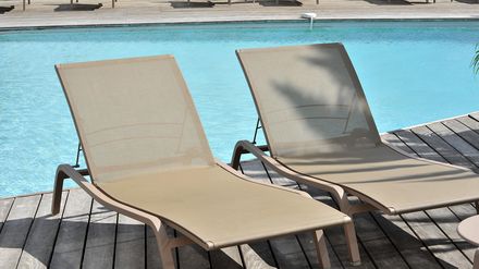 Zwei leere Sonnenliegen stehen auf einer Holzterrasse direkt an einem Hotelpool.