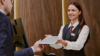 Ein Hotelgast nimmt an der Rezeption ein Tablet entgegen.