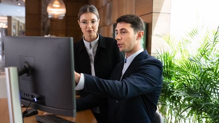 Zwei Hotelmitarbeiter schauen auf einen Computer an der Rezeption