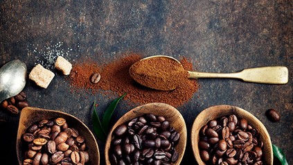 Verschieden Sorten Kaffeebohnen in Schüsseln und Kaffeepulver auf einem Löffel