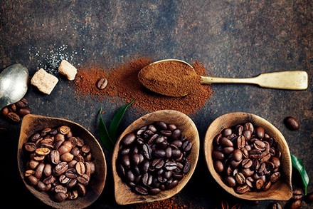 Verschieden Sorten Kaffeebohnen in Schüsseln und Kaffeepulver auf einem Löffel