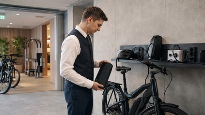 Hotelmitarbeiter prüft einen E-Bike-Akku an einer Ladestation in einem modernen Fahrradraum.