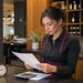 Gastronomie-Mitarbeiterin prüft an einer Restauranttheke einen Dienstplan; neben ihr stehen eine Uhr und ein Taschenrechner.