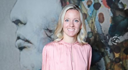Porträt von Anna Heuer in rosafarbener Bluse vor einer farbig gestalteten Wand