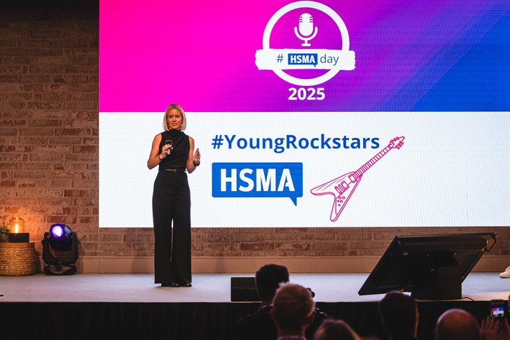 Anna Heuer spricht beim HSMAday 2025 vor einer Bühnenwand mit dem Schriftzug YoungRockstars.