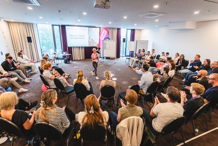 Teilnehmende sitzen während der Sessionplanung im Kreis um eine Sprecherin.