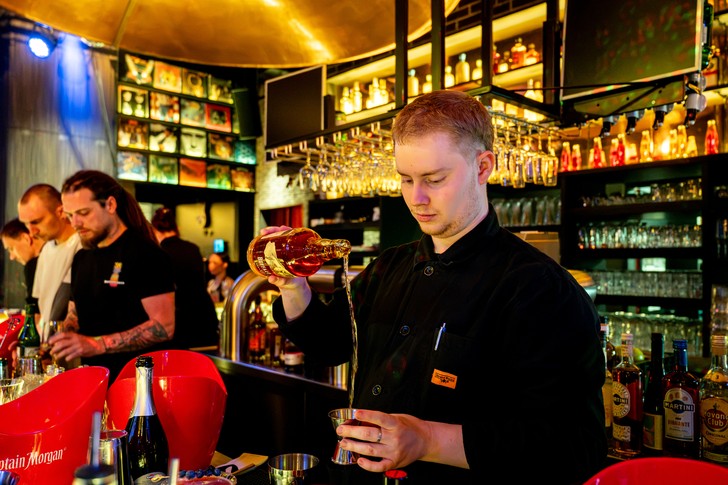 Ein Bartender gießt eine braune Flüssigkeit aus einer Flasche in einen Messbecher.