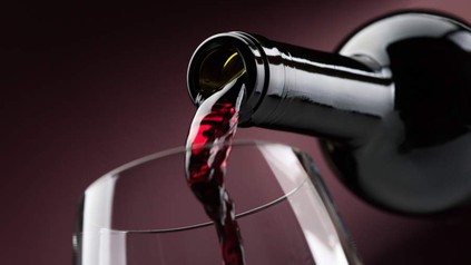 Rotwein wird von der Flasche in ein Glas gegossen