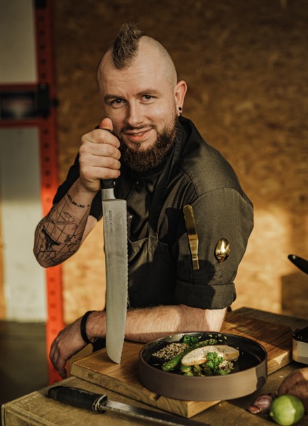 Koch Frank Schirmacher mit schwarzer Kochkleidung und Messer in der Hand.