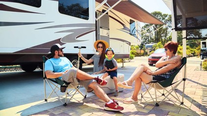 Ein paar Personen sitzen in Campingstühlen vor einem Wohnwagen