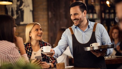 Happy waiter serving coffee to young women in a cafe.