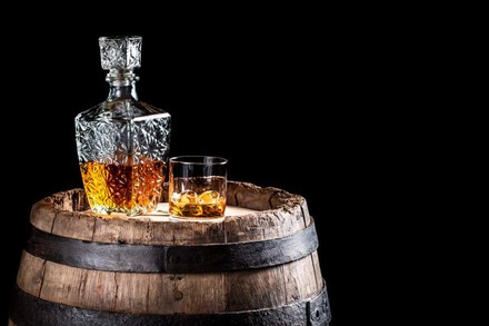 Ein Whiskeyglas und eine Flasche stehen auf einem alten Holzfass