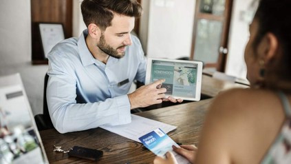 Eine Dame im Reisebüro lässt sich von einem Mitarbeiter mit einem Tablet beraten
