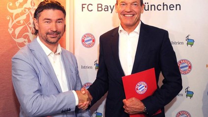 Denis Ivošević und Andreas Jung reichen sich die Hand vor einem Banner auf dem offizieller Partner des FC Bayern München steht