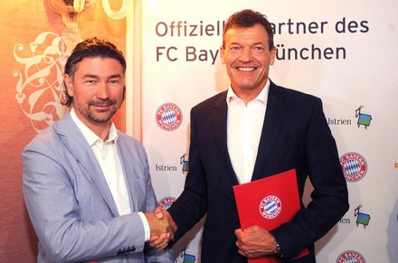 Denis Ivošević und Andreas Jung reichen sich die Hand vor einem Banner auf dem offizieller Partner des FC Bayern München steht