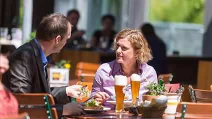 Mann und Frau sitzen zum Mittagessen in einem Gastgarten bei einem Weizenbier.