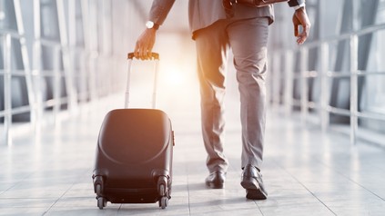 Geschäftsreisender im Anzug, der einen Rollkoffer zieht