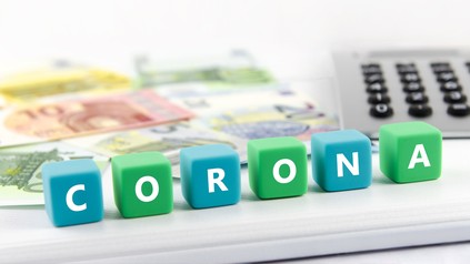 Würfel mit der Aufschrift Corona vor Geldscheinen und einem Taschenrechner