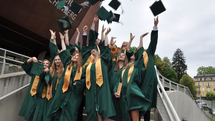 Absolventen in grünen Roben werfen ihre Kappen in die Luft