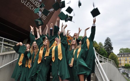 Absolventen in grünen Roben werfen ihre Kappen in die Luft