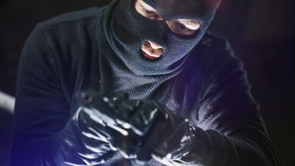Einbrecher sieht auf seine Waffe