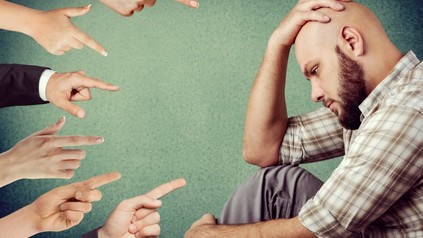 Mann mit Glatze sieht betrübt aus, mehrere Finger deuten auf ihn