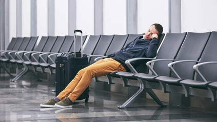 Ein Mann schläft allein in einer Wartehalle mit seinem Koffer
