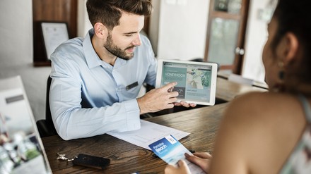 Rezeptionist im Hotel zeigt einer Frau etwas auf einem Tablet