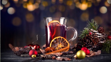 Tasse Glühwein, die von Gewürzen und Weihnachtsdeko umgeben ist