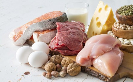 Verschiedene Lebensmittel wie Fleisch, Lachs, Eier, Nüsse und Käse auf einem Holzbrett angerichtet