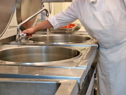 Eine Küchenhilfe am Wasserhahn in einer Küche