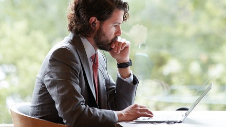 Mann im Anzug mit Kopfhörern sitzt nachdenklich vor einem Laptop