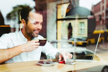 Mann trinkt Kaffee und sieht auf sein Smartphone