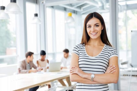Eine junge Frau steht lächelnd vor einem Besprechungstisch in einem modernen Büro