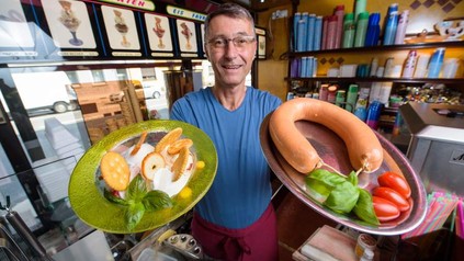 Ein Mitarbeiter präsentiert in der einen Hand Eis und in der anderen eine Wurst