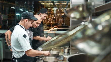 Kochschule, ein erfahrener Koch begutachtet die Arbeit zweier Jungköche