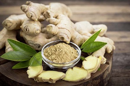 Ein Holzscheit auf dem ganzer Ingwer, Ingwerscheiben und Ingwergewürz angerichtet sind