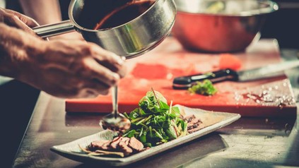 Koch träufelt Soße über Fleisch