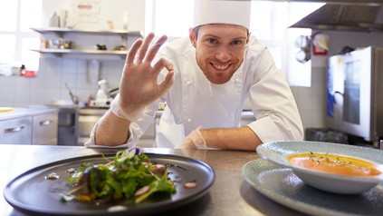Koch präsentiert lächelnd seine Speisen in der Küche