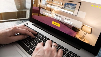 Zwei Hände tippen auf einem Laptop auf dem eine Buchungswebseite für Hotels aufgerufen ist