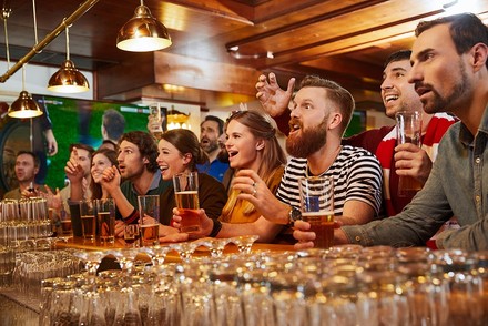 Viele Menschen sitzen in einer Bar und jubeln mit Bier in den Händen