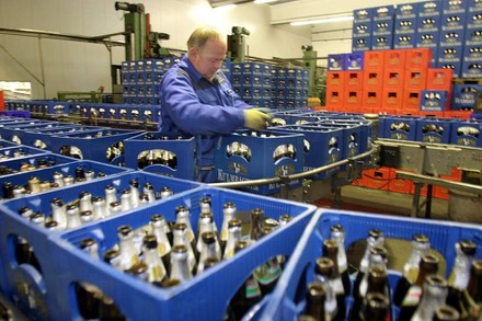 Ein Mitarbeiter steht inmitten hunderter Bierkästen mit Leergut und stapelt diese auf ein Laufband