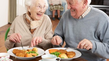 Zwei ältere Menschen sitzen lachend vor einem Teller mit gesundem Essen