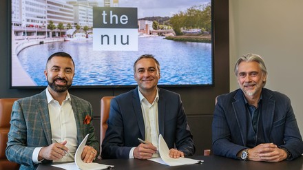 Drei Männer sitzen vor einem Tisch und unterzeichnen einen Vertrag; the niu Hotel