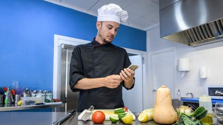 Ein Koch blickt in der Küche auf sein Smartphone