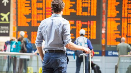 Ein Reisender mit Koffer steht vor einer Anzeigetafel im Flughafen
